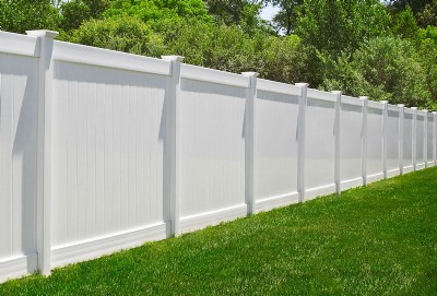 White vinyl fence installation in yard with green tree leaves in the background